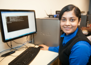 Student smiling at camera while working at a computer displaying a command-line window.