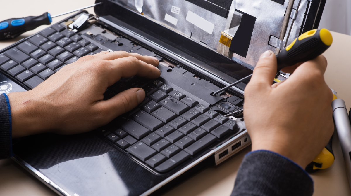 Person repairing a laptop keyboard with screwdrivers.