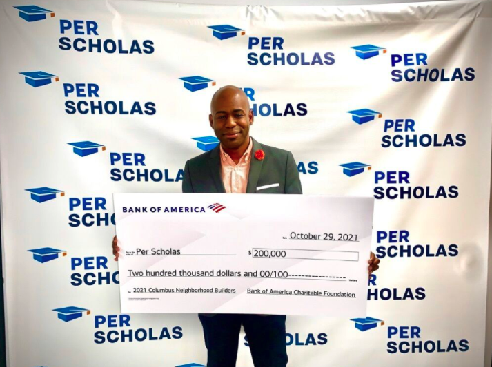 Man holding an oversized ceremonial check for $200,000 made out to Per Scholas from Bank of America Charitable Foundation, standing in front of a Per Scholas step-and-repeat backdrop.