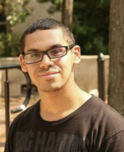 Young adult smiling at camera in an outdoor setting.