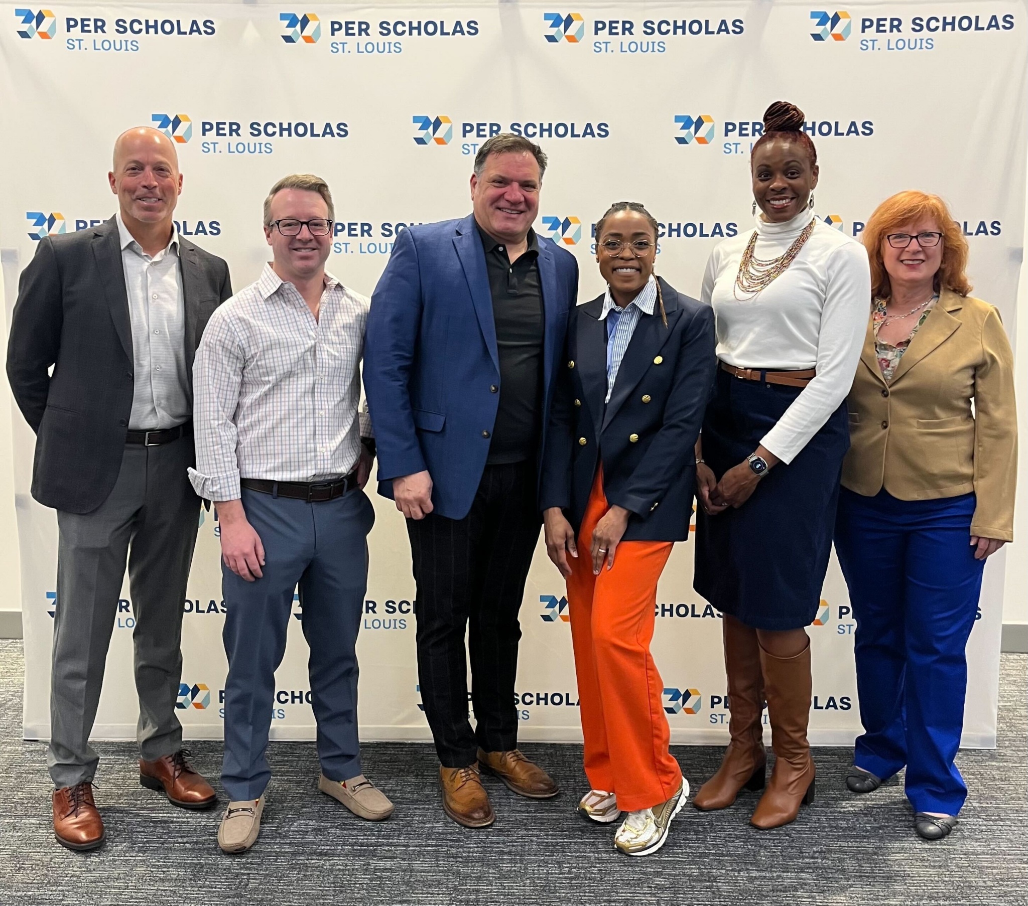 Six smiling adults stand shoulder-to-shoulder in front of a Per Scholas St. Louis step-and-repeat banner at an event.