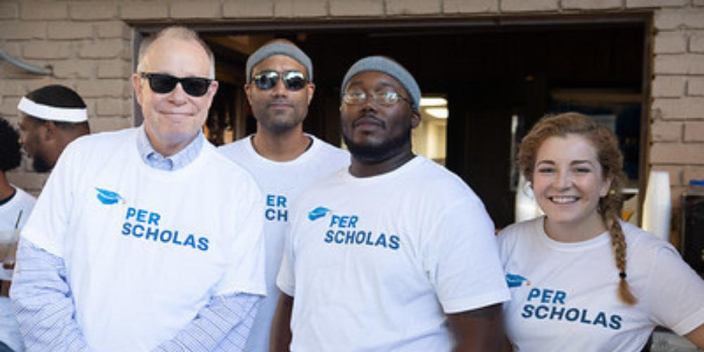 Four adults wearing Per Scholas t-shirts stand together and smile for a group photo.