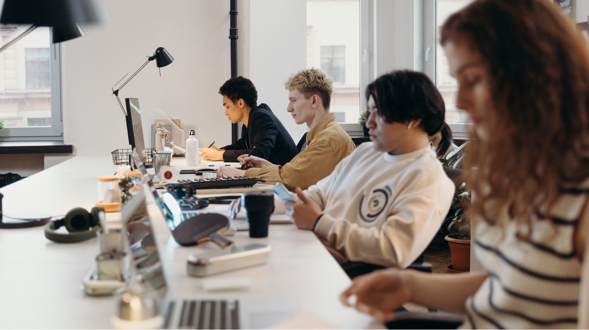 A group of learners working at a shared workspace, each focused on individual tasks on laptops.