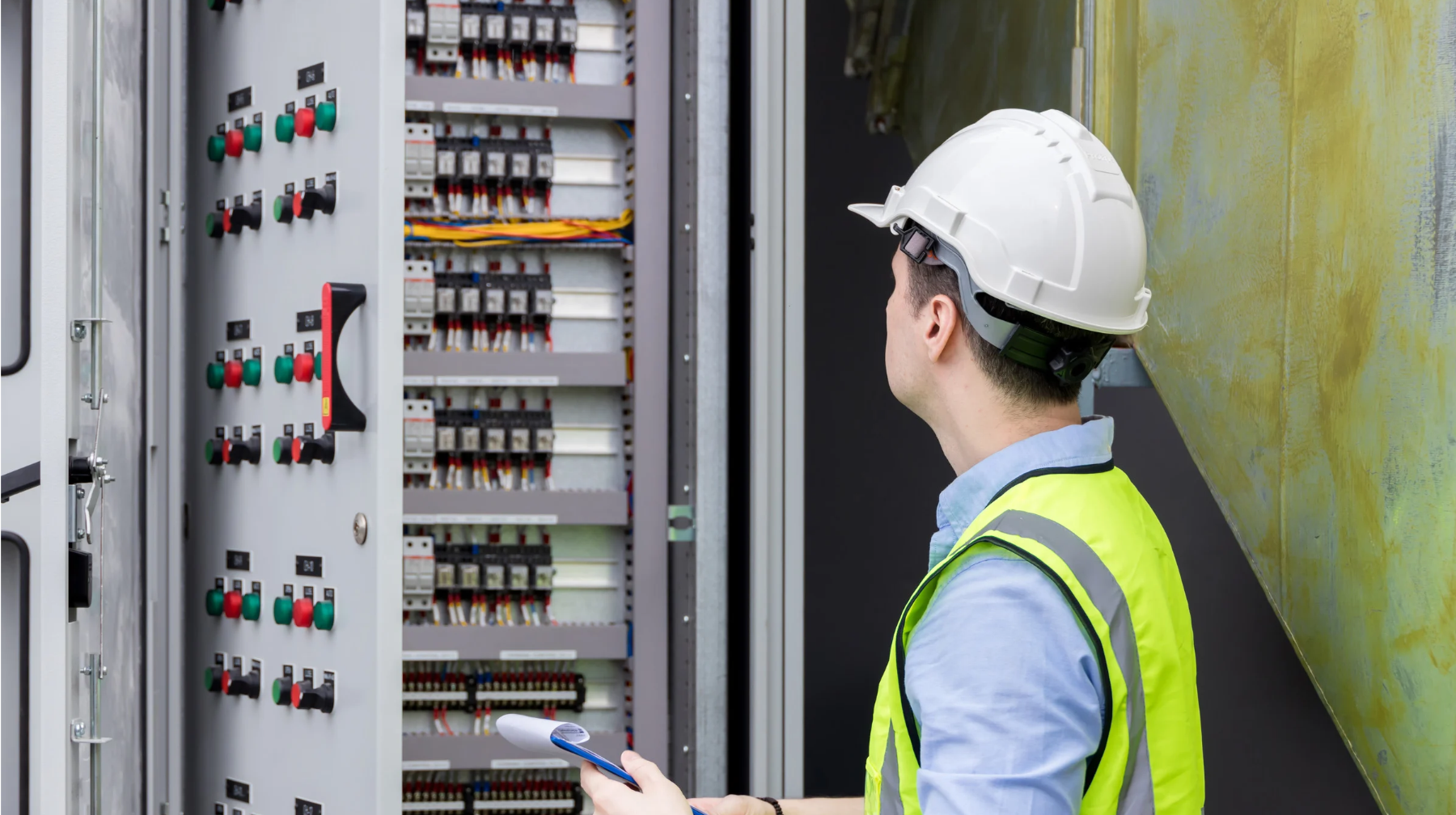 Technician in a hard hat inspecting an electrical control cabinet with breakers and relays