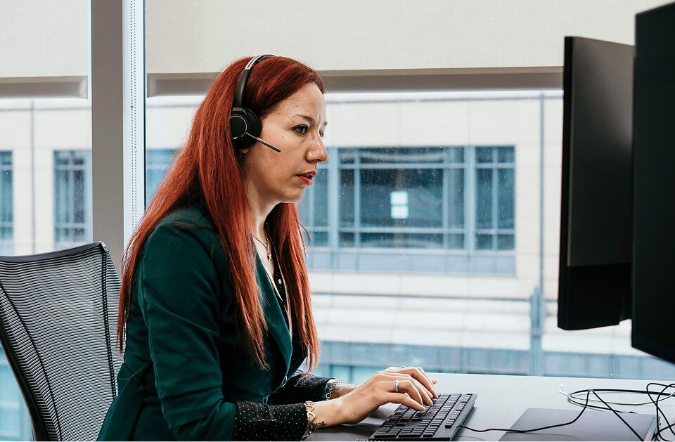 Employee seated at desk with headset looking at computer