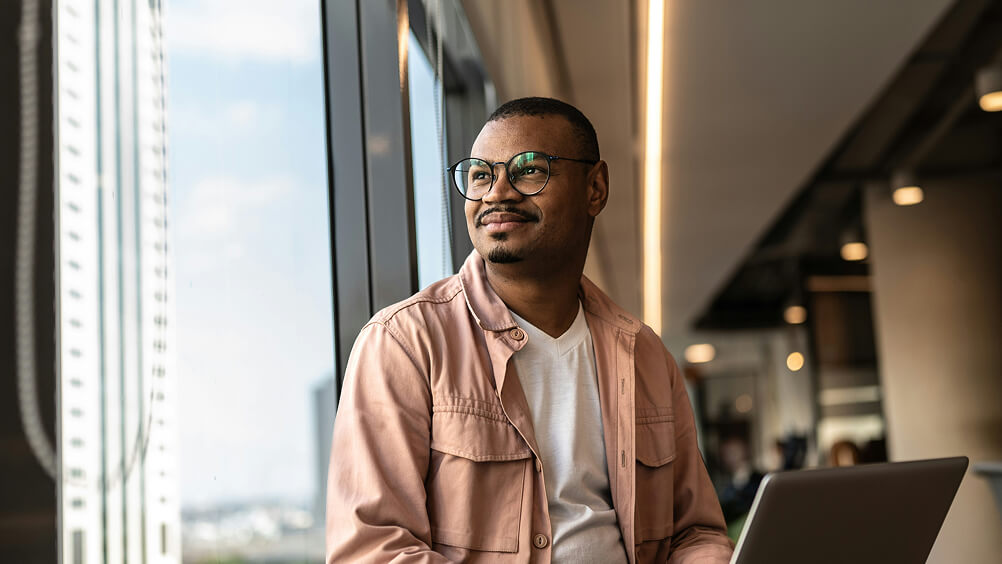 Employee with laptop in office looking out window