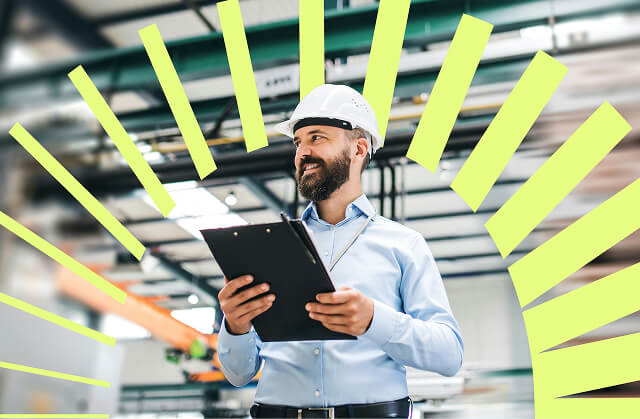 Male engineer wearing a hard hat holding a clipboard and smiling in a manufacturing facility.