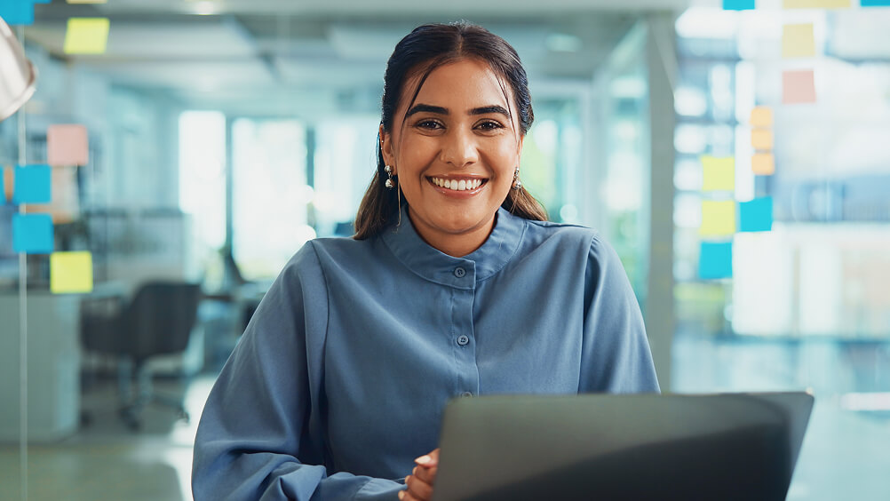 Portrait of employee in office workspace at desk with laptop