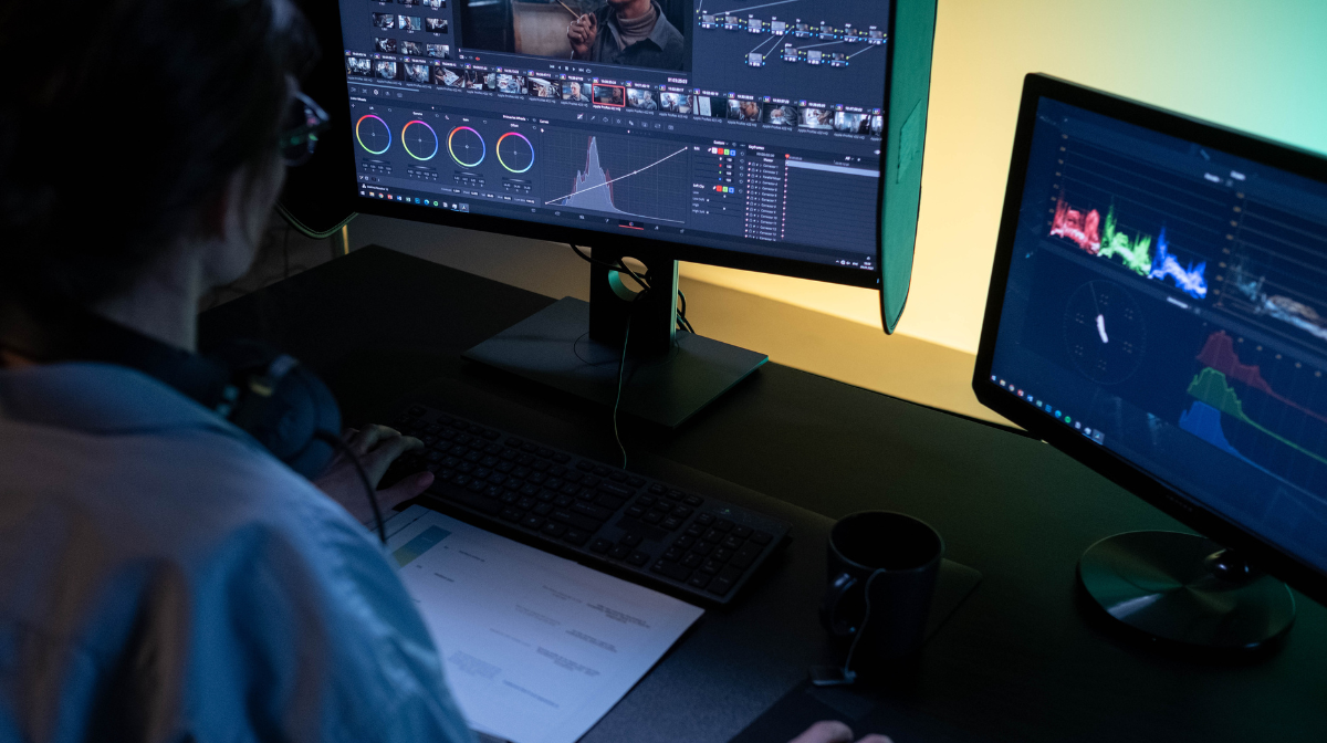 Person working at a dual-monitor editing workstation in a dark setting.