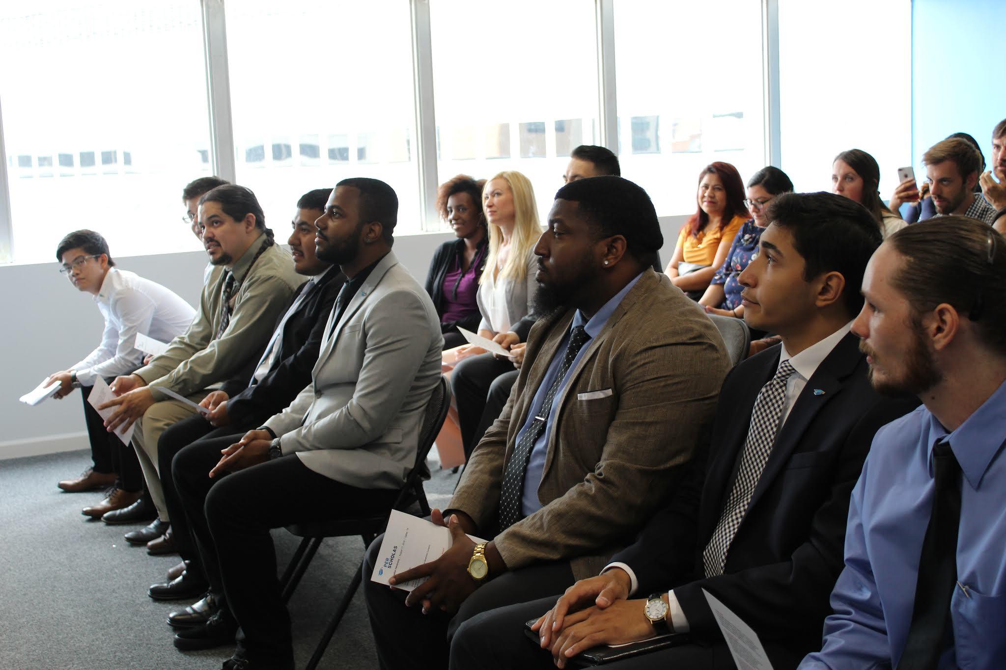 A diverse group of adult learners seated in rows listening attentively in a classroom event.