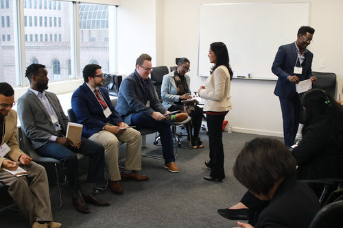A small group of adult learners and an instructor stand and sit in a classroom.