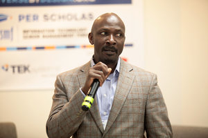 Man speaking into a microphone at a Per Scholas networking event.