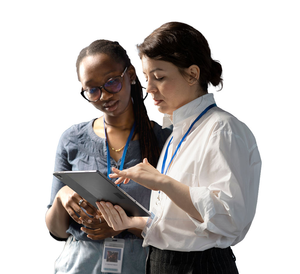 Two professional women wearing ID badges review a tablet together, conveying focused collaboration and teamwork