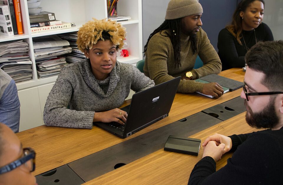 A group of people gathered around a table, collaborating on laptops in an office setting.