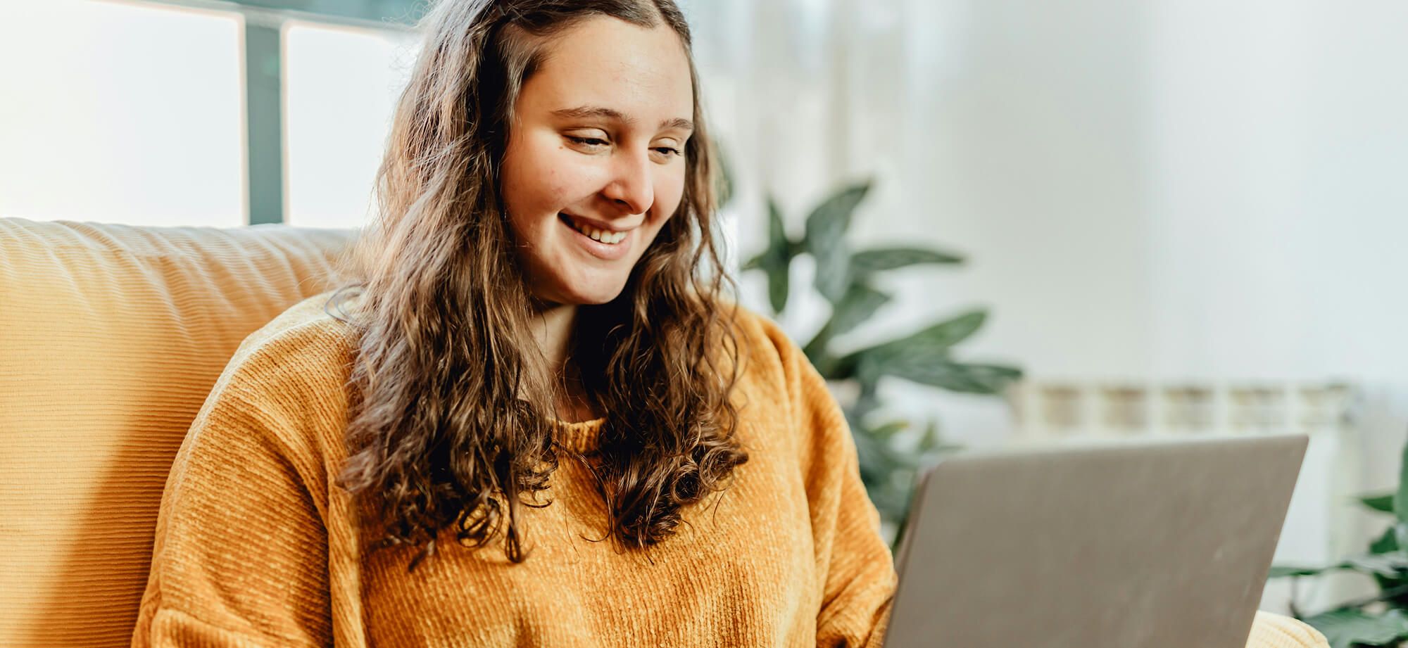 Woman seated at couch in workspace with laptop