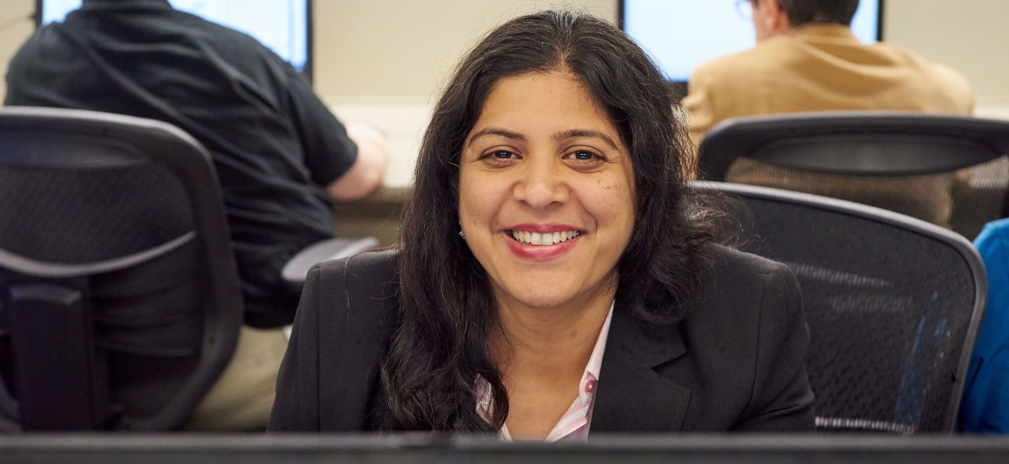 Portrait of woman student smiling and sitting in computer room with classmates 