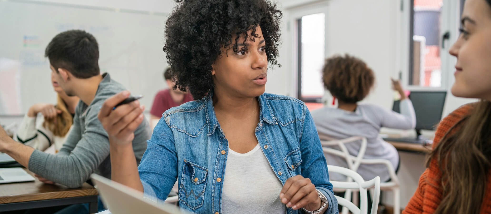 Woman teaching in classroom with student seated at desk with computer