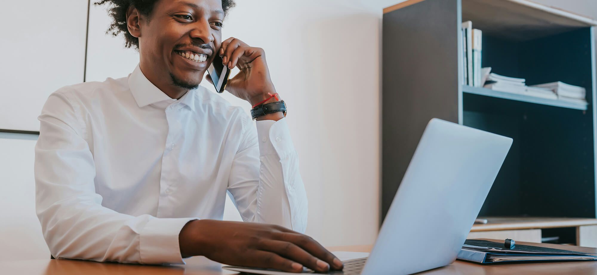 Man at home looking at computer while using cell phone