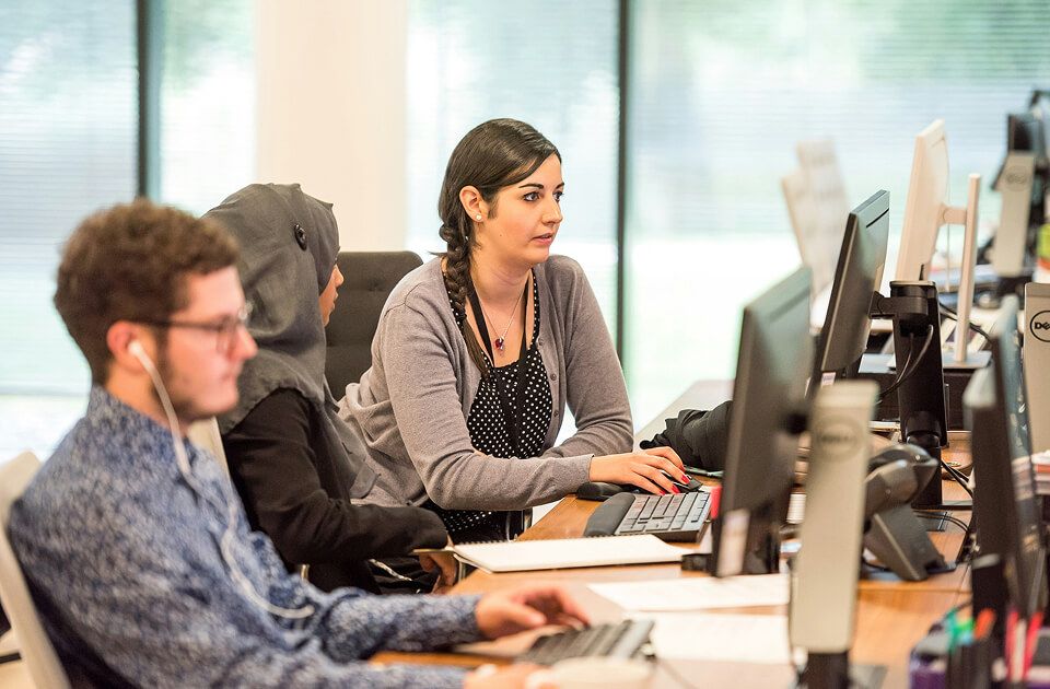 Three coworkers focused on computer monitors at desks in an open office.
