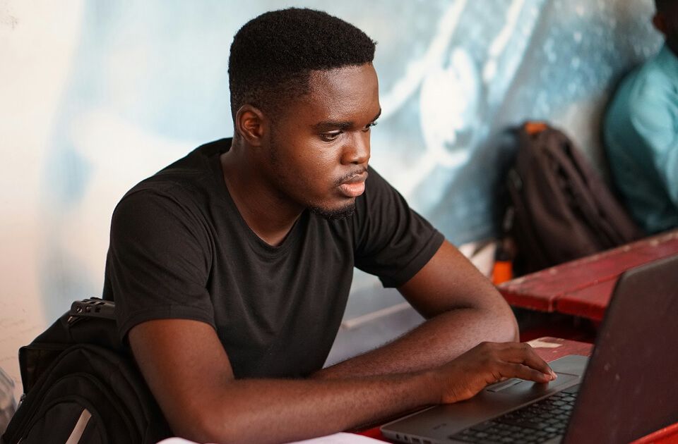 Young man with short black hair, wearing a black t-shirt, focused on typing on a laptop.