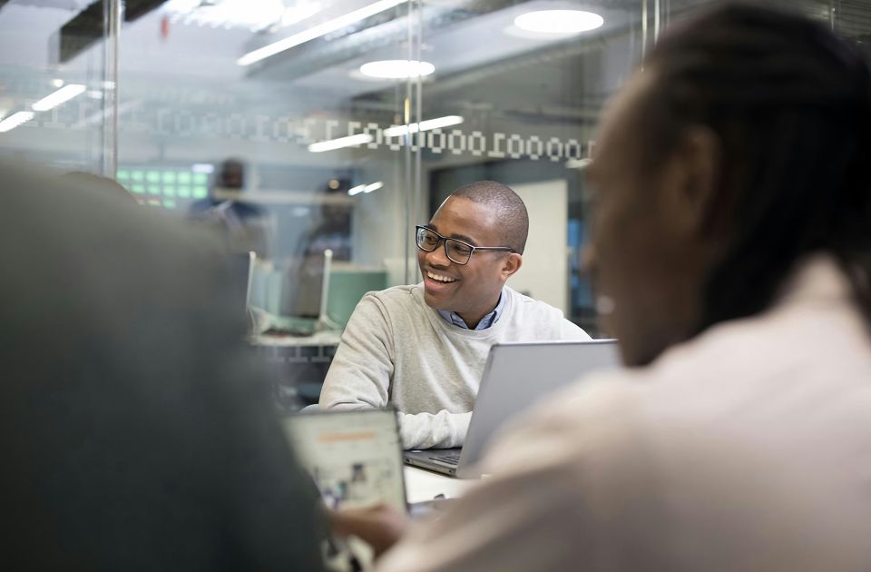 Young male professional sitting in meeting in front of a laptop.