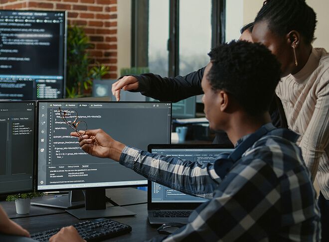 Two working professionals in office setting looking at code on computer monitors