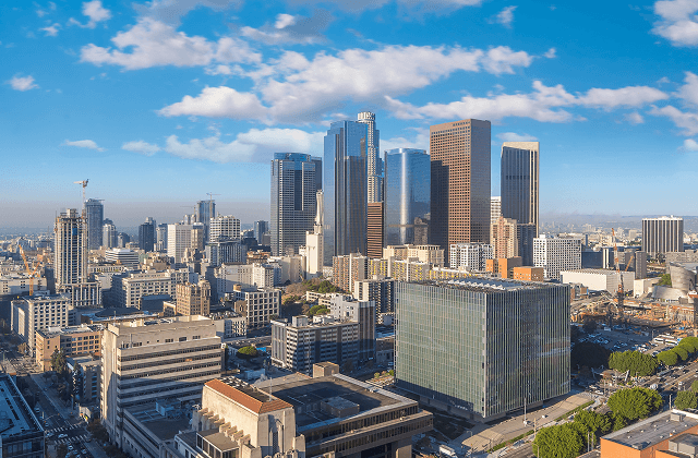 Downtown Los Angeles skyline with modern high-rise towers under a bright blue sky with clouds.