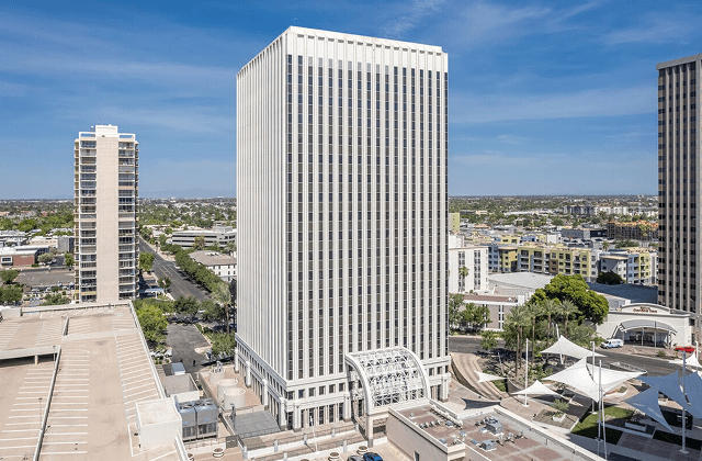 View of a high-rise office building in downtown Phoenix, surrounded by buildings, and city streets under a clear blue sky.