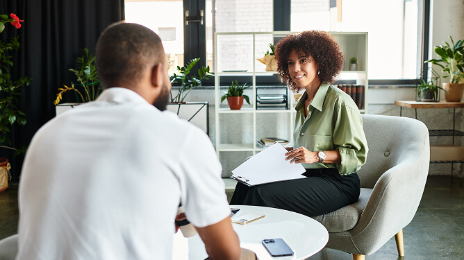 Male and female young professionals in an office meeting, one reviewing papers while speaking with the other.