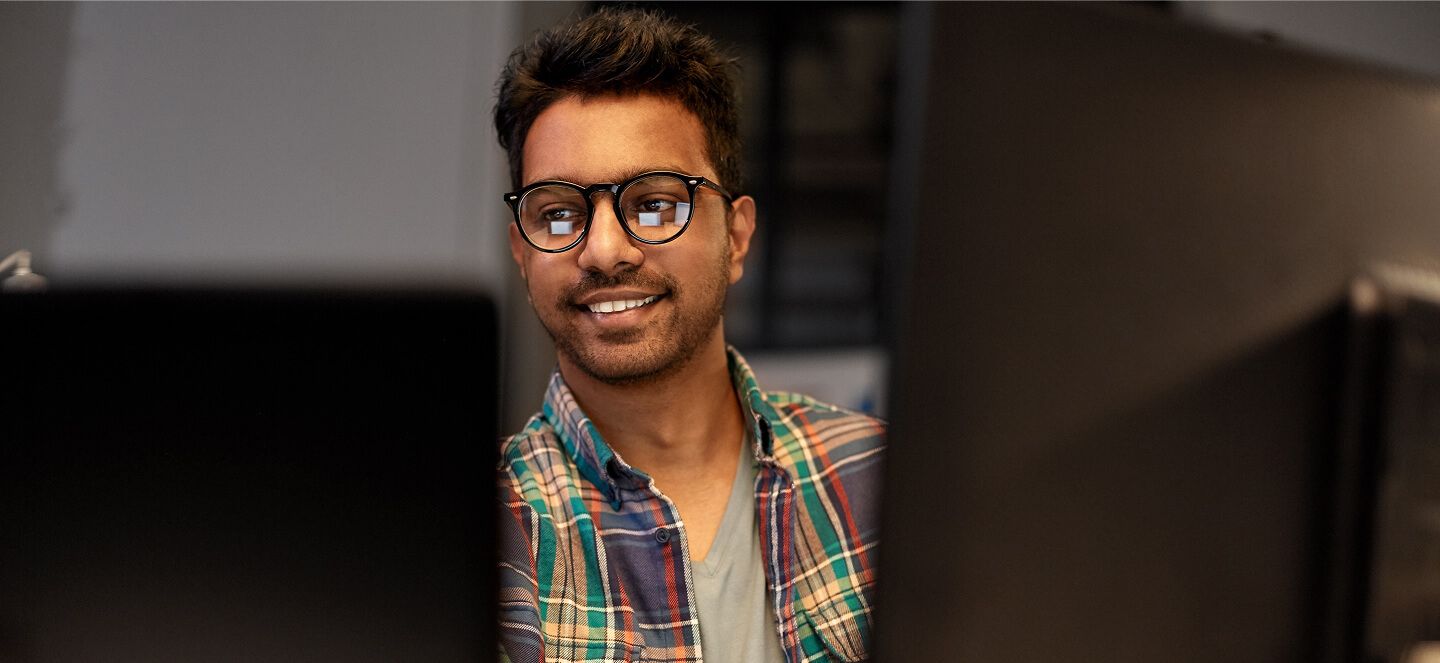 Man coding on multiple computer desktops in office