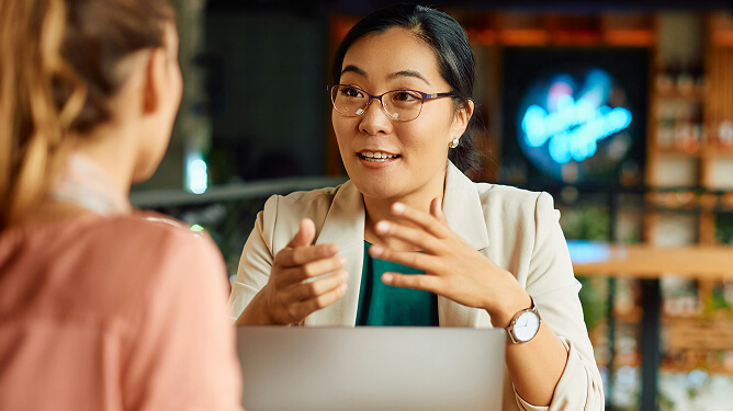Mentor speaking and gesturing while advising a student across a laptop.