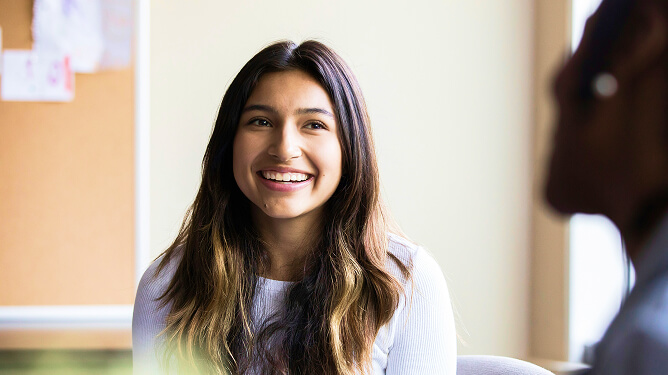 Young woman smiling as she speaks with another person.