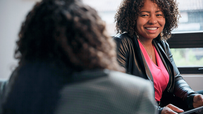 Two adults in a one-on-one conversation, one smiling and engaged while listening to the other.