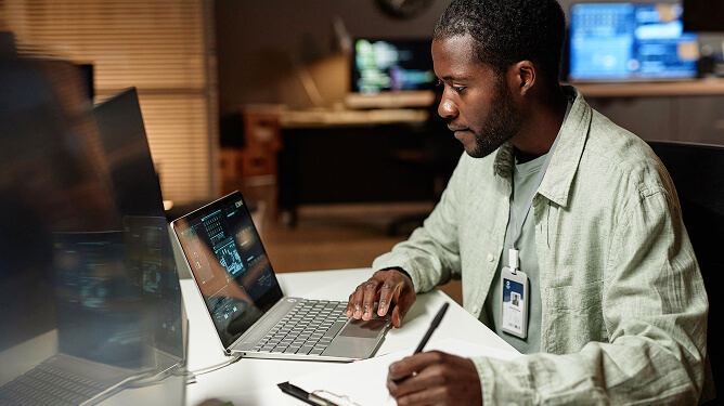 Man working intently at a laptop in a tech workspace.
