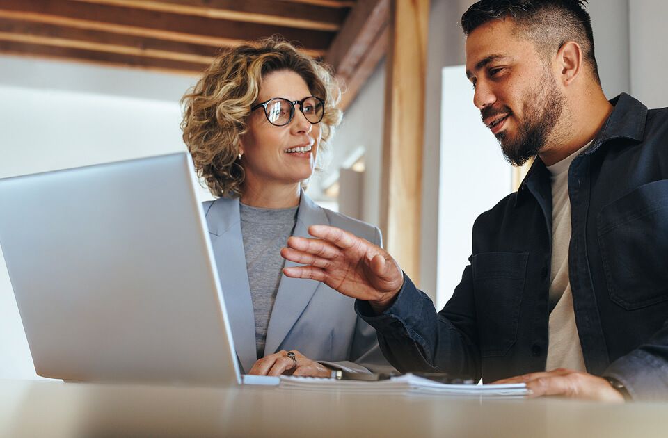 Two professionals collaborating at a laptop in an office setting.